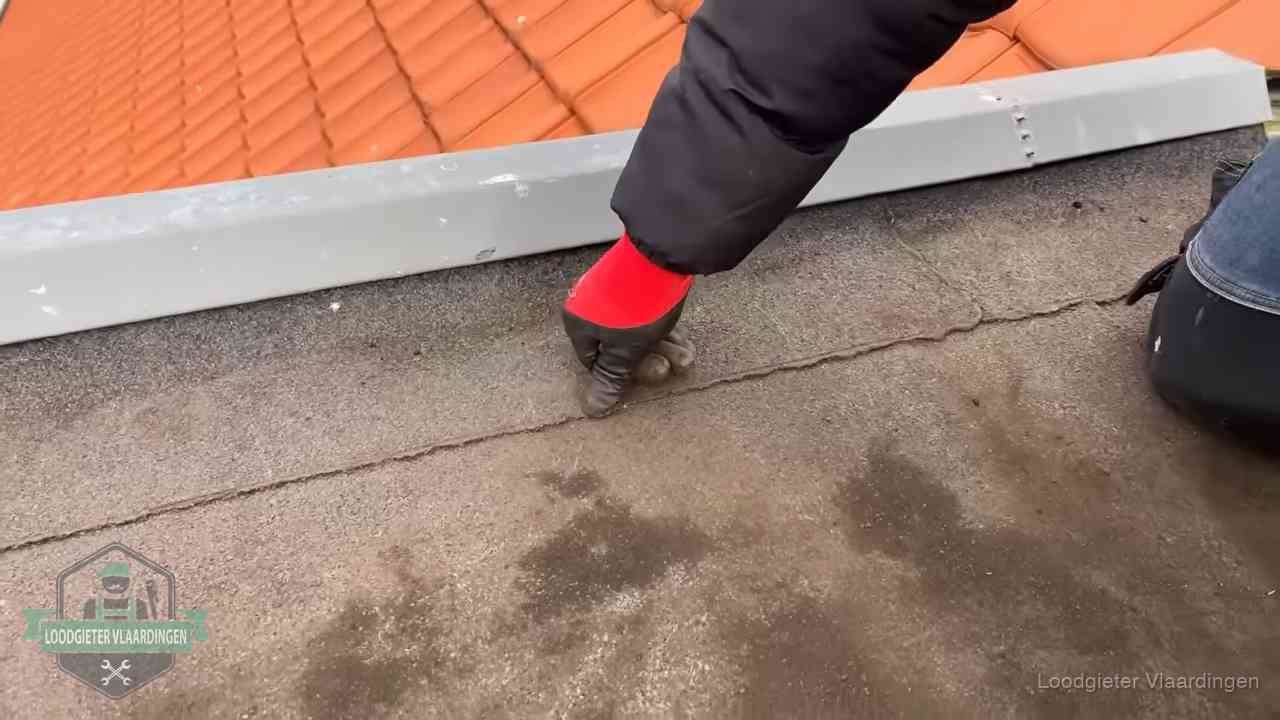 Vakman wijst een naad met vochtplekken aan op een bitumen plat dak in Vlaardingen