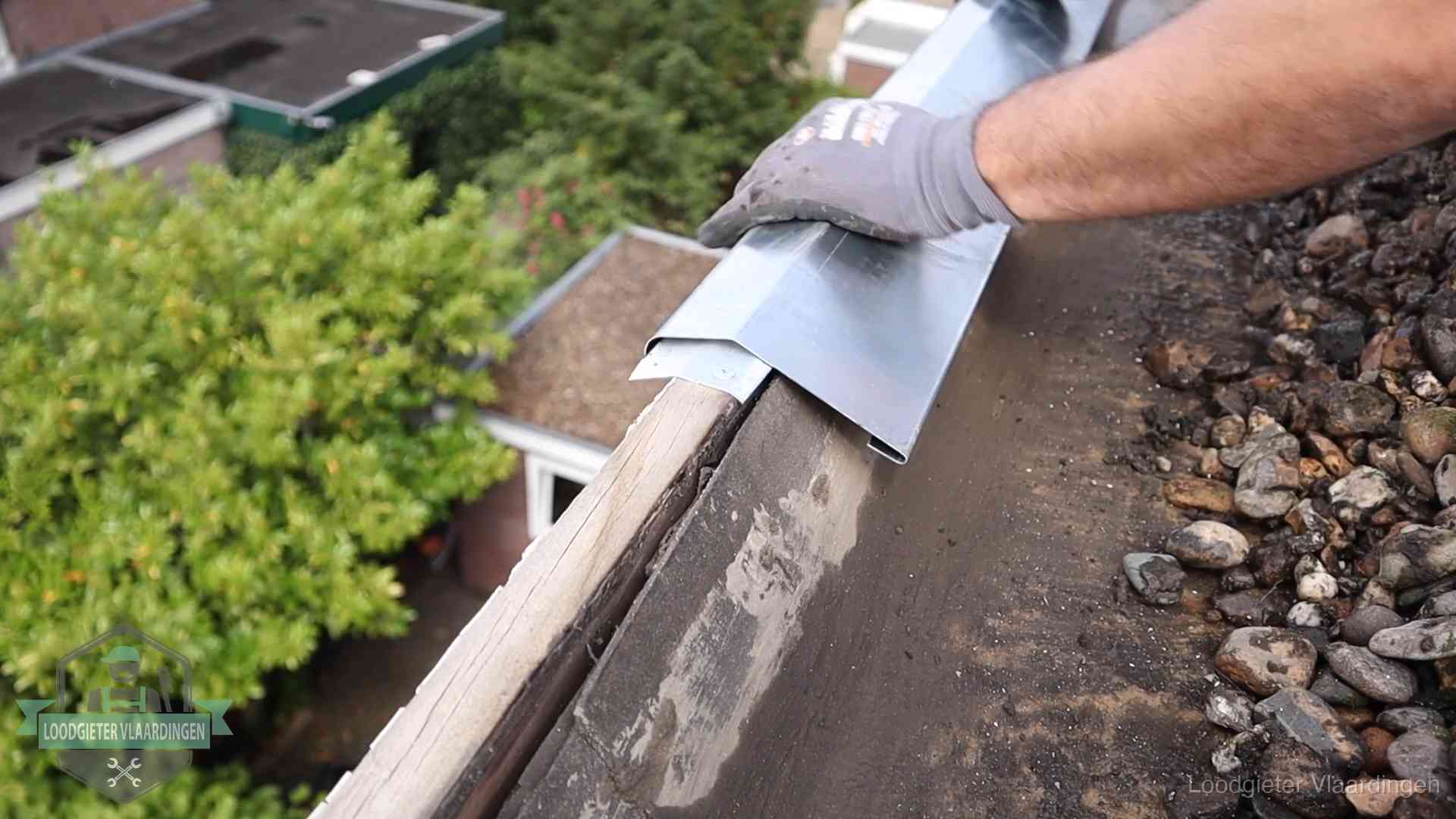Dakdekker plaatst een zinken deklijst op een dakrand met uitzicht over een woonwijk in Vlaardingen