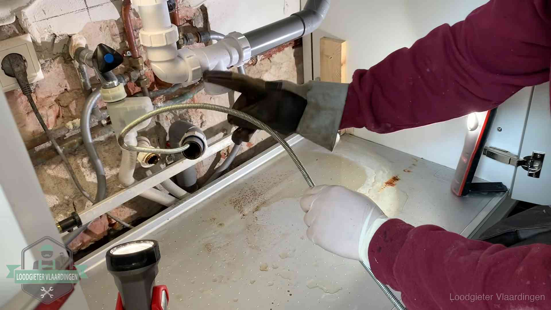Ontstoppingsveer gaat in een geopende sifonaansluiting onder het aanrecht in Vlaardingen